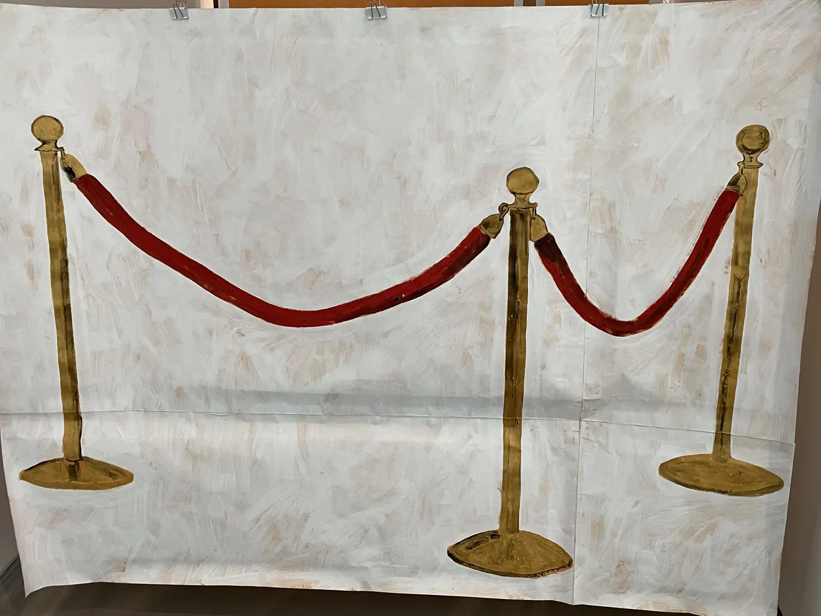 A painted backdrop of a red velvet rope strung between gold stanchions